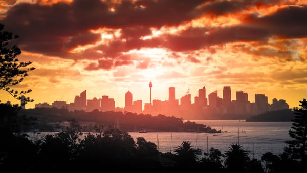 A striking sunset over Sydney's skyline, with the silhouette of the city's iconic structures outlined against the vibrant hues of the evening sky. This image complements the blog post's topic on navigating the time difference between Sydney and Perth while travelling and experiencing the distinct moments each city offers.