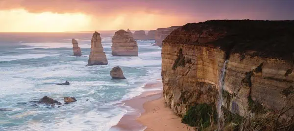 A breathtaking view of the Twelve Apostles at sunset along the Great Ocean Road, with towering limestone formations and rugged cliffs. This image captures the awe-inspiring beauty of coastal Victoria and encourages readers to explore Australia and its iconic natural landmarks.