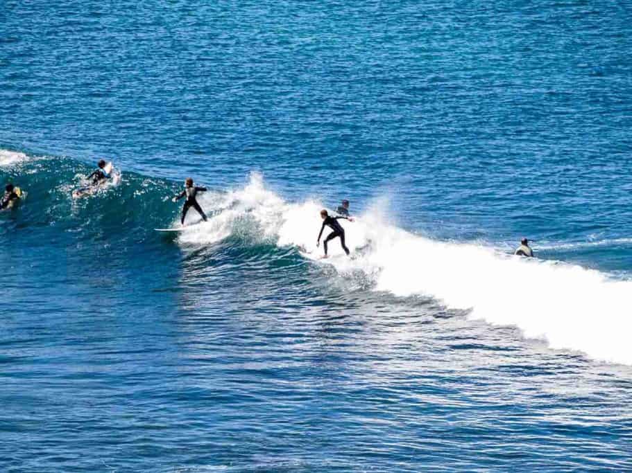 Surfers riding and paddling through clear blue waves at one of the best surf beaches in Australia, showcasing the dynamic surfing scene at Bells Beach.