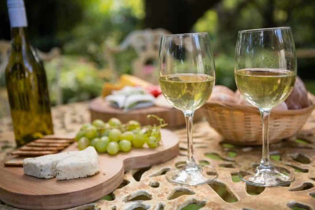 Two glasses of chilled white wine on a rustic table, with cheese and grapes, set in a lush garden, evoking the relaxed ambiance of Hunter Valley wine tours from Sydney.