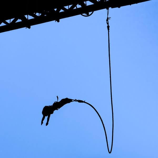 A bungee jumper captured in mid-leap, silhouetted against the blue sky, reminiscent of the exhilarating experience of bungee jumping on Sydney Harbour Bridge.