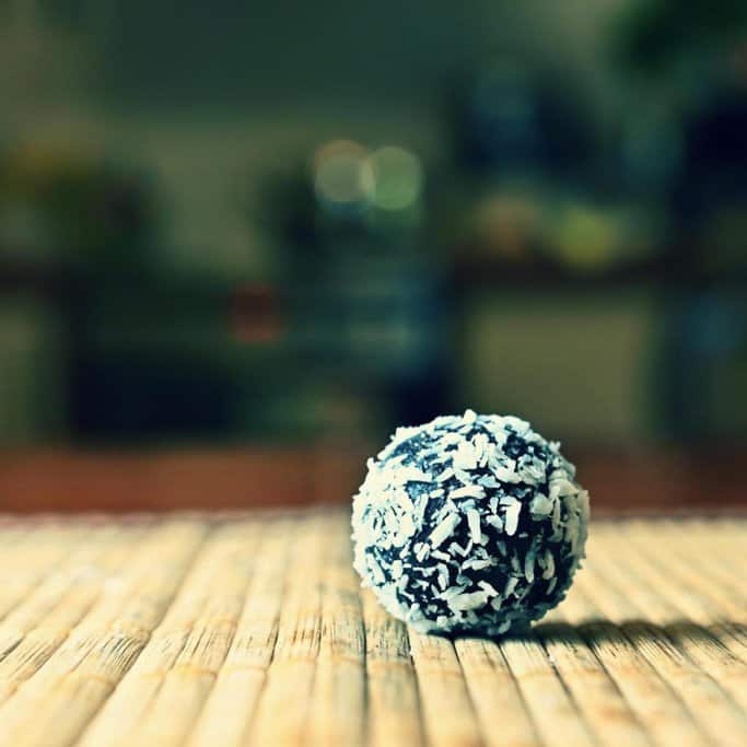A single rum ball coated in shredded coconut, a classic no-bake treat popular during Christmas desserts in Australia, displayed on a wooden surface.