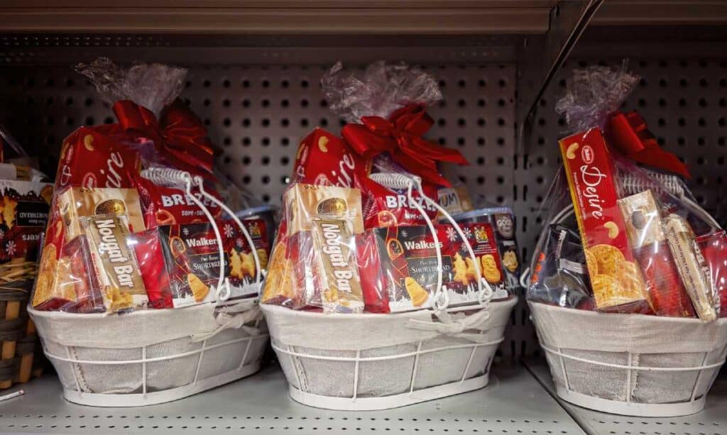Three white Christmas hampers filled with various festive treats like nougat bars, shortbread, and biscuits, wrapped in clear plastic with red bows. These hampers represent popular gift ideas for Christmas in Australia, showcasing an assortment of snacks that are commonly found in Australian Christmas hampers.