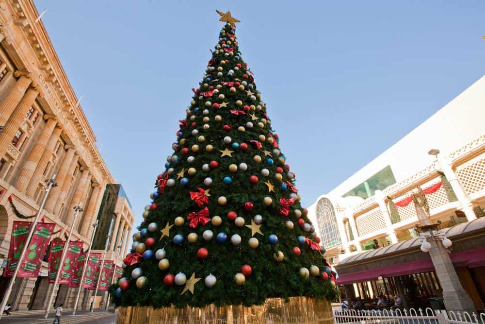 Large decorated Christmas tree in the Perth CBD, adorned with red, gold, and blue ornaments under a clear blue sky. Represents the festive decorations and holiday celebrations central to Christmas in Perth.
