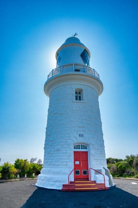 Cape Naturaliste Lighthouse against a clear blue sky, built in 1903 with red doors, symbolizing the enduring history and maritime significance of the region.