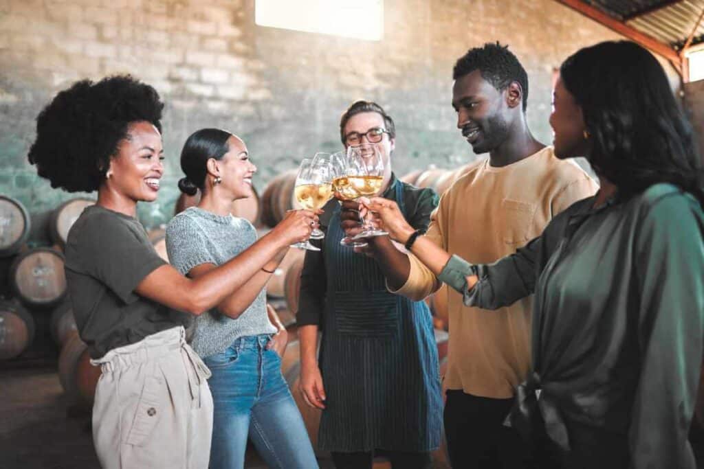 A group of friends clinking glasses in a toast, sharing a joyful moment during a winery tour in Hunter Valley, with oak barrels in the background.