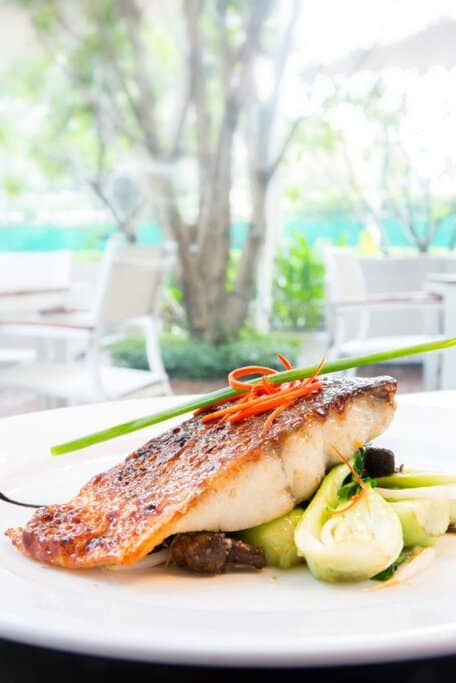 A beautifully plated grilled barramundi fillet with crispy skin, served with fresh vegetables and garnishes. This popular Aussie seafood dish showcases the rich flavours of iconic Australian cuisine, often enjoyed in coastal regions.