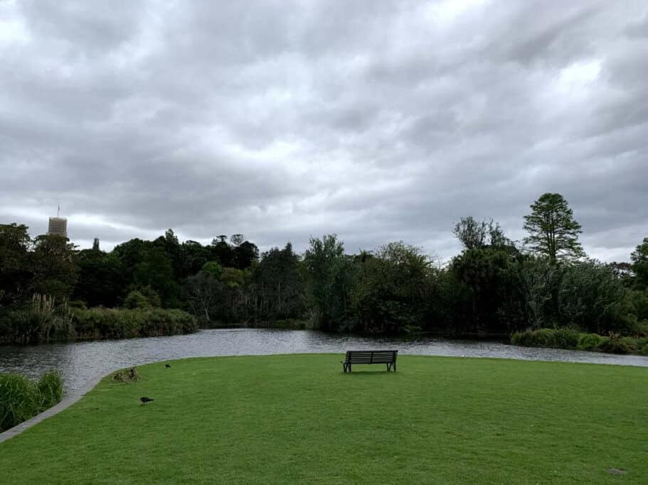 A peaceful scene at Fitzroy Gardens in Melbourne, featuring a solitary bench facing a calm body of water surrounded by lush greenery. This tranquil spot is one of Melbourne’s most Instagrammable places, perfect for capturing serene and picturesque moments.