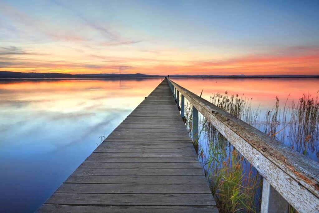 Long Jetty at Tuggerah Lake, New South Wales, showcasing a peaceful sunset over calm waters. Though scenic, Tuggerah Lake is sometimes considered one of the worst beaches for swimming in Australia due to poor water quality and high levels of algae, making it less ideal for beachgoers.