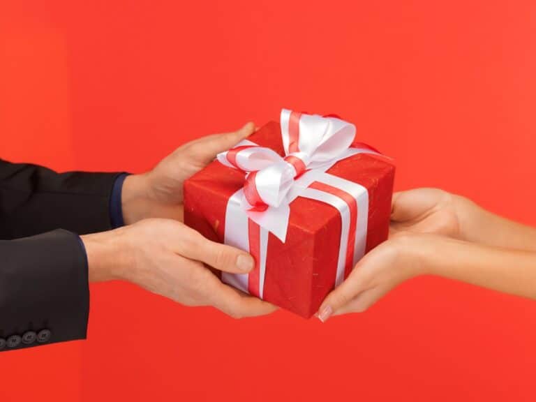 Man handing a red gift box with a white bow to a woman, representing a thoughtful exchange of Christmas presents for men, highlighting meaningful gift ideas for the holiday season.