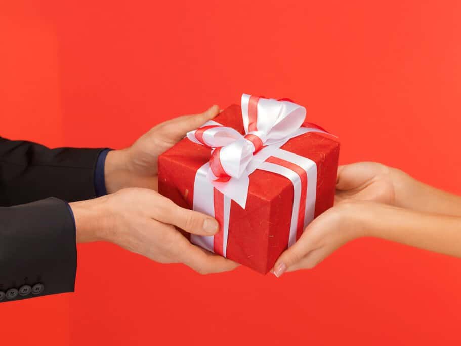 Man handing a red gift box with a white bow to a woman, representing a thoughtful exchange of Christmas presents for men, highlighting meaningful gift ideas for the holiday season.