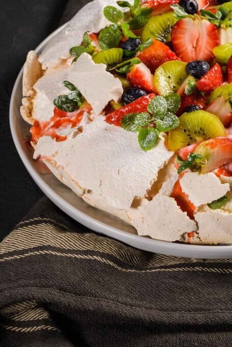 A homemade pavlova topped with fresh strawberries, kiwi, blueberries, and mint, showcasing its crisp meringue shell and soft, marshmallow-like centre. This classic dessert is a favourite in Australian cuisine and one of the most iconic Aussie foods..