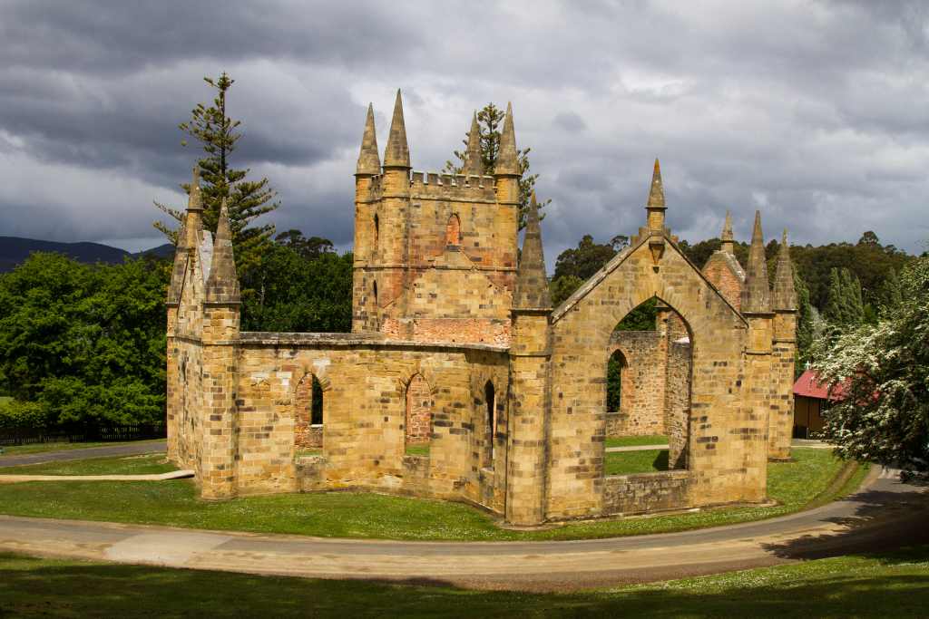 A wide view of the Port Arthur Historic Site showing the preserved ruins surrounded by green lawns and tall trees, with blue skies above - what you need to know about Port Arthur is how stunning and peaceful the landscape feels, blending history with natural beauty.