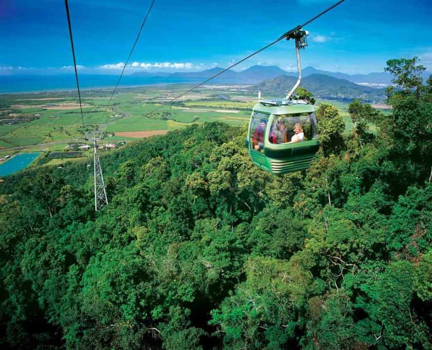 Cable car gliding over the lush rainforest canopy with a panoramic view of the landscape near Cairns, offering a unique perspective for those exploring the natural beauty on a Cairns travel adventure.