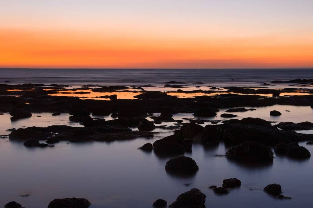 Sunset at East Point in Darwin, with calm waters and scattered rocks creating a serene coastal view. This image reflects the tranquil outdoor lifestyle that many consider when weighing the benefits and drawbacks of living in Darwin.